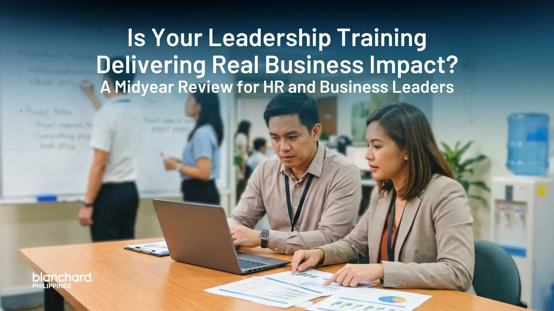 Two corporate professionals collaborate in a modern office, analyzing financial charts and data on a laptop to review the measurable business results of their leadership development strategy.